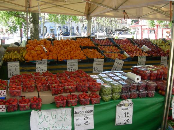 Outdoor fruit stall with strawberries, oranges and apples under a white canopy