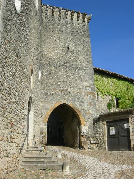 Medieval stone tower with arched gateway, cobblestone streets, green ivy, blue sky
