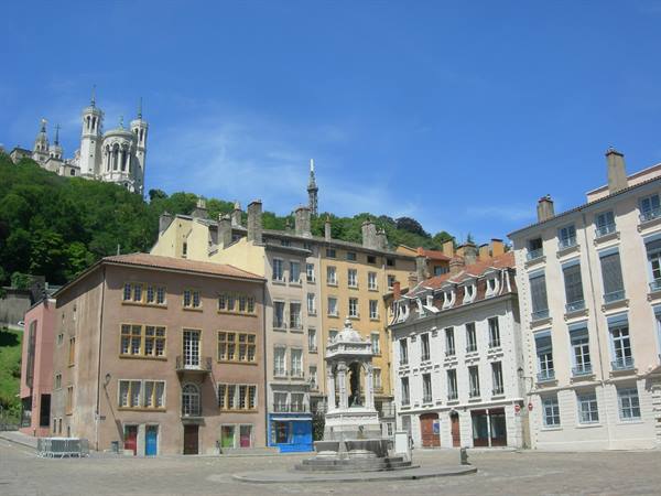 Lyon square with stone fountain and Fourvière basilica on the hill