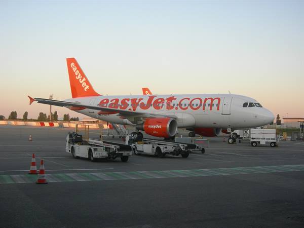 Orange and white easyJet plane towed on the apron, with traffic cones and ground vehicles