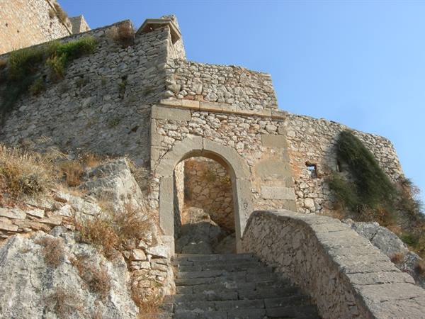 Stone staircase leading to arched gate of ancient fortress, rugged walls under blue sky