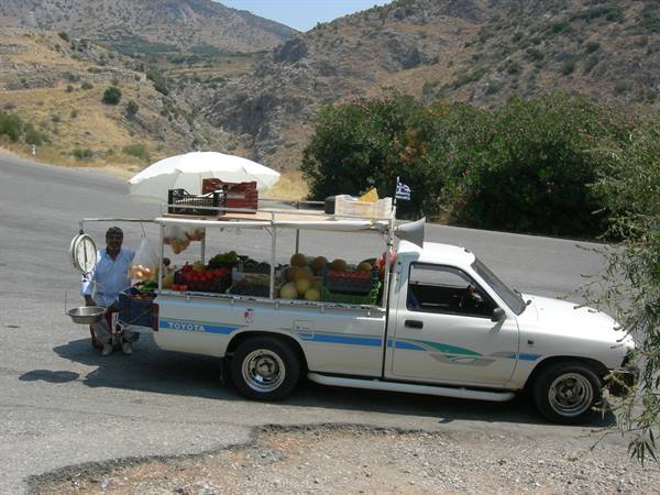 fruit vendor beside a white Toyota pickup loaded with vegetables on mountain road