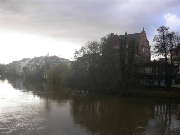 River with houses and a dark red brick building under cloudy sky