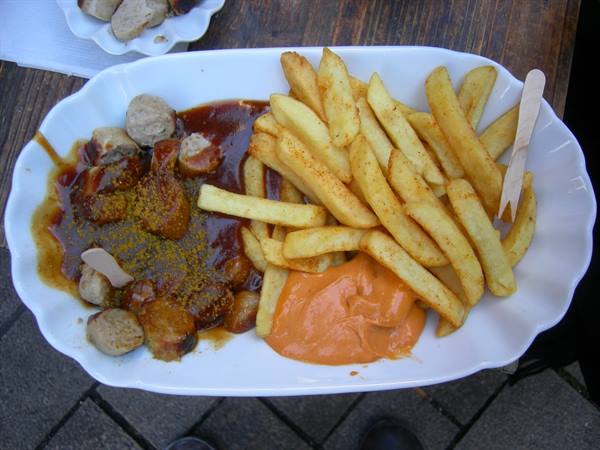 Sliced currywurst with ketchup, fries and curry powder on white plate