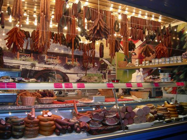 Market cold cuts stall: hanging sausages under light bulbs, chilled counter below