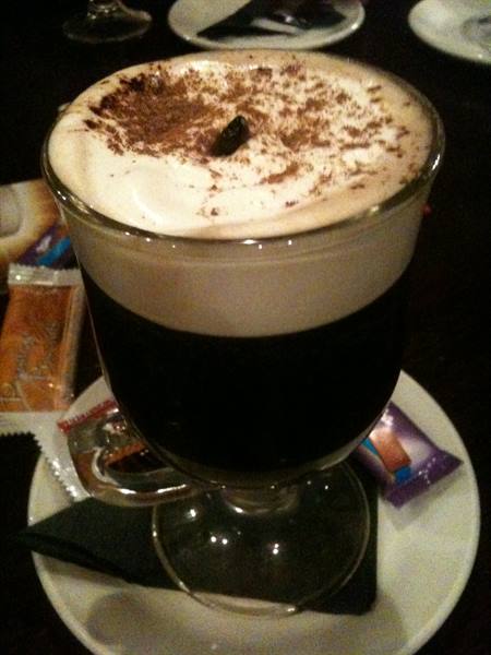 Irish coffee with cream and cocoa in a glass, warm bar lighting