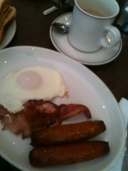 English breakfast: fried egg, bacon and sausages on plate, tea cup