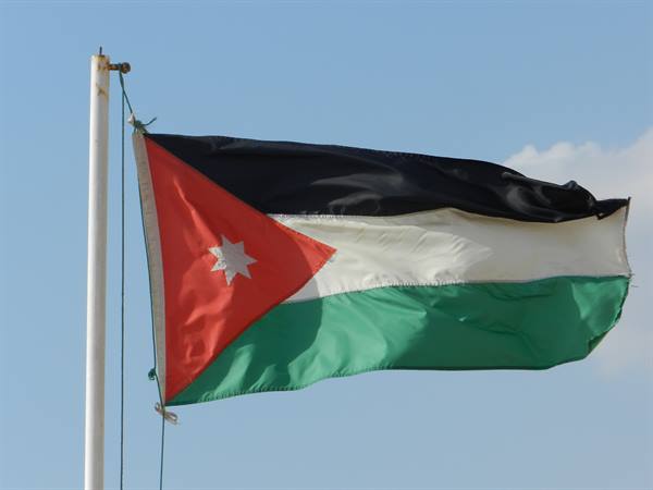 Jordanian flag with white star waving on a pole against a blue sky