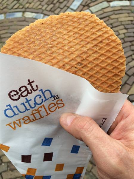 Hand holding a wrapped Dutch stroopwafel, cobblestone pavement below