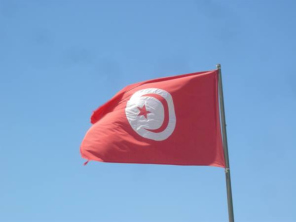 Tunisian red flag with crescent and star waving against blue sky