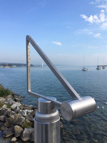 Steel measuring gauge on Geneva lakeside, sailboats and lighthouse on the water