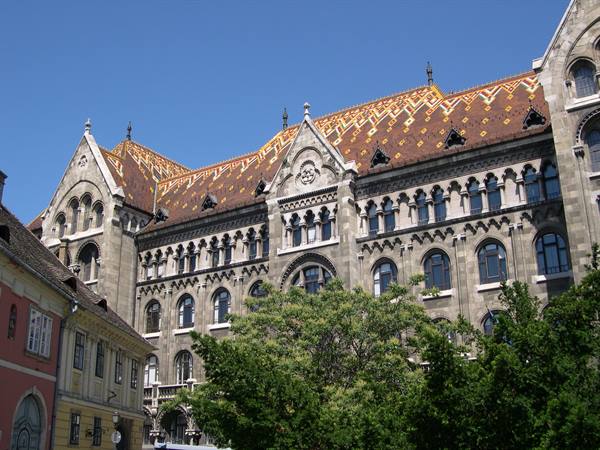 Vajdahunyad Castle in Budapest, neo-Gothic stone facade with patterned colorful roof, green trees