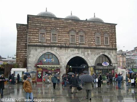 People with umbrellas in front of the stone Spice Bazaar under rain