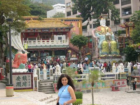 Smiling woman in front of Kwun Yam shrine, colorful statues and visitors