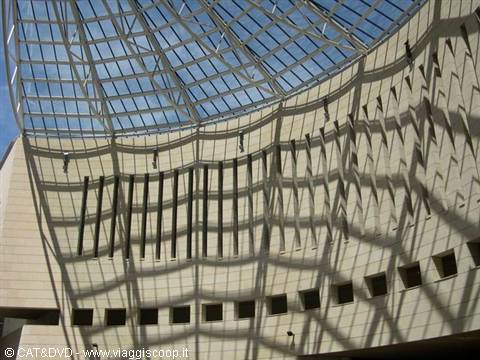 Glass and steel dome casts geometric shadows on curved stone facade