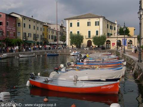 Colorful boats moored in Lazise harbor, yellow and pink houses overlooking the water