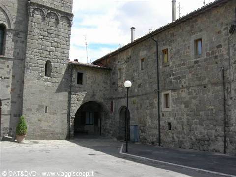 Grey stone buildings with arch, Romanesque bell tower, lamp post on sunny square