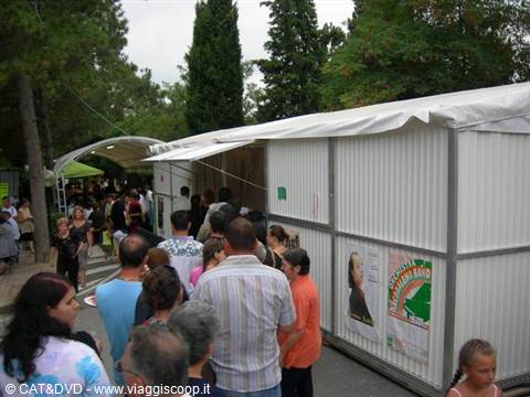 Visitors queueing outside a white corrugated metal shed among tall trees