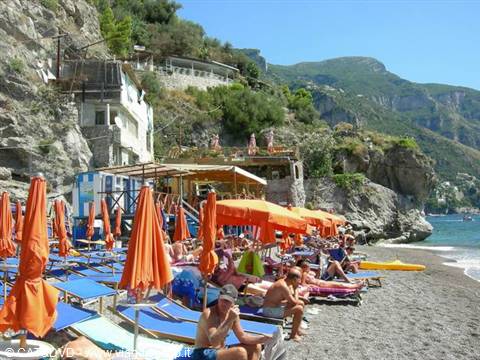 Beach with orange umbrellas and sun loungers, people on dark sand