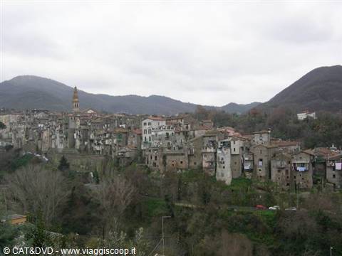 Old stone hill village with bell tower, houses and bare trees under grey sky