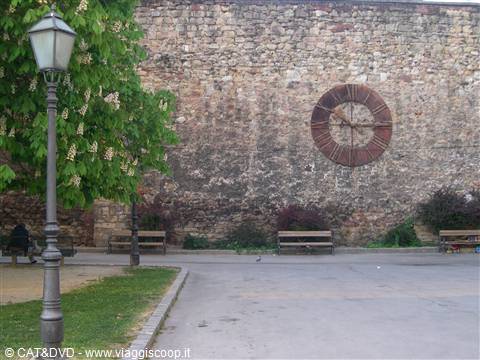 Iron clock on old stone wall, benches and lamppost in the park