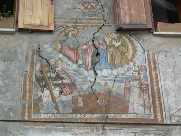 Cracked 1658 sacred fresco on plastered wall between wooden shutters