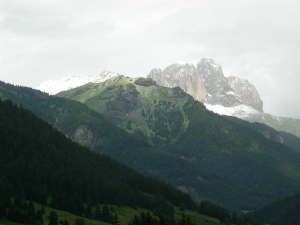 Dolomites: snowy rocky peaks above forested slopes under cloudy sky