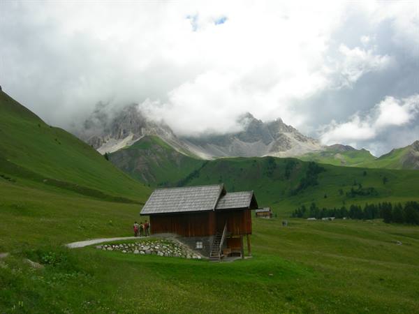 Wooden huts on green meadows, Dolomite peaks wrapped in clouds