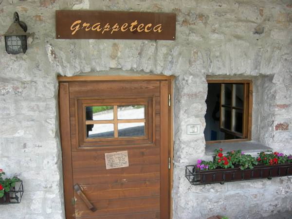 Wooden Grappeteca sign above wooden door on stone wall, colorful flowers