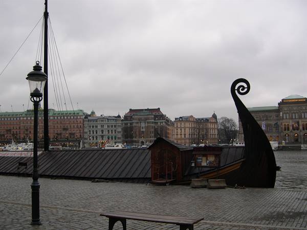 Wooden Viking ship moored on Stockholm waterfront, grey sky, lamppost and buildings