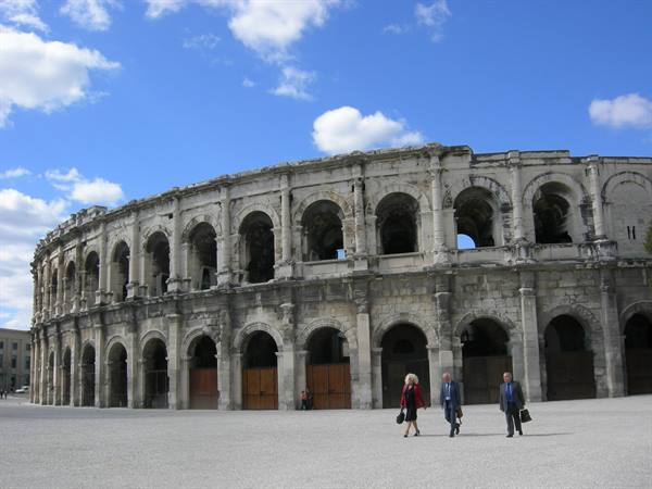 Three pedestrians walk past the Roman stone amphitheater of Nîmes