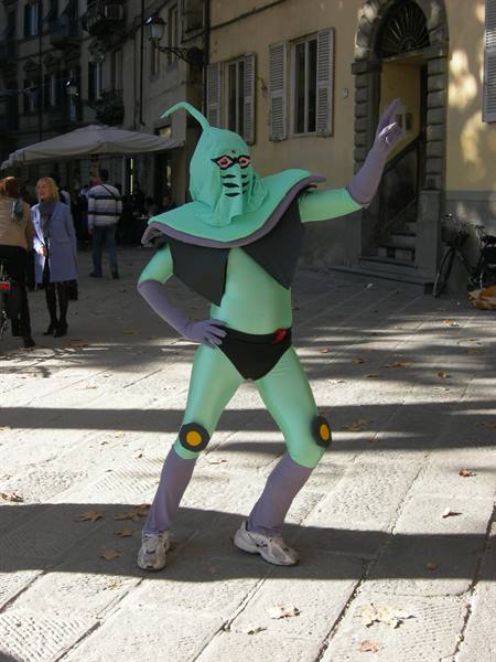 Cosplayer in green alien costume poses in a sunny stone-paved square