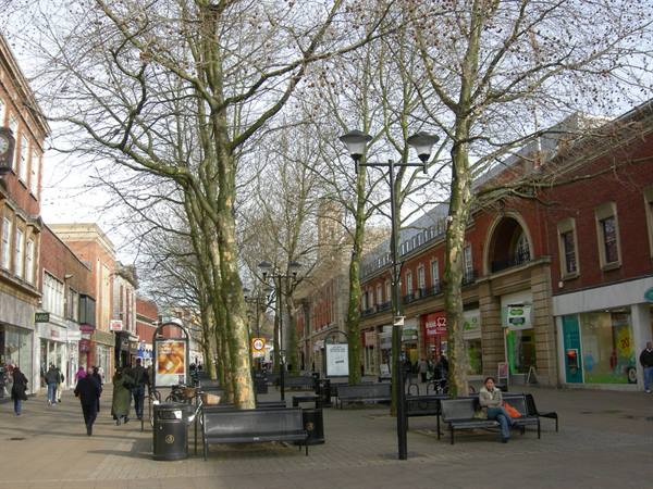 Pedestrian shopping street with bare trees, benches and walking people