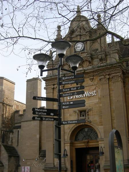 Stone building with clock and NatWest sign, black street signpost in front