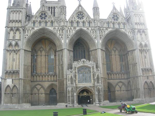 Gothic facade of Peterborough Cathedral, green lawn and lawn mower tractor