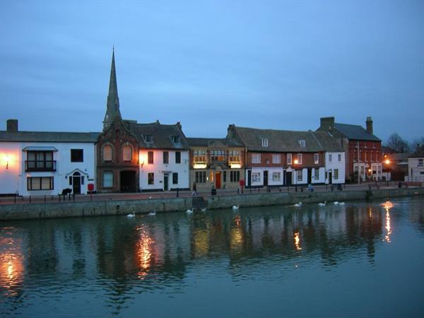 Colourful riverside houses with church spire, lights glowing at dusk
