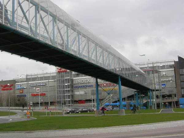 Glass and blue steel footbridge in front of shopping mall, grey sky