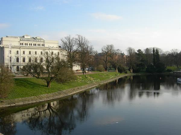 White historicist palace reflected in the canal, bare trees and grassy bank in Malmö