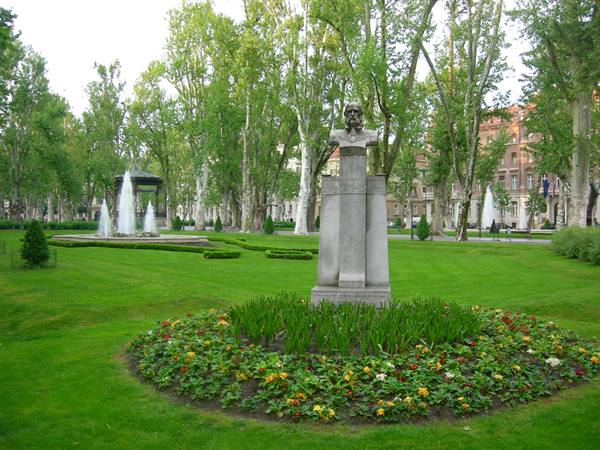 Stone bust on pedestal in city park, flowerbeds and fountains