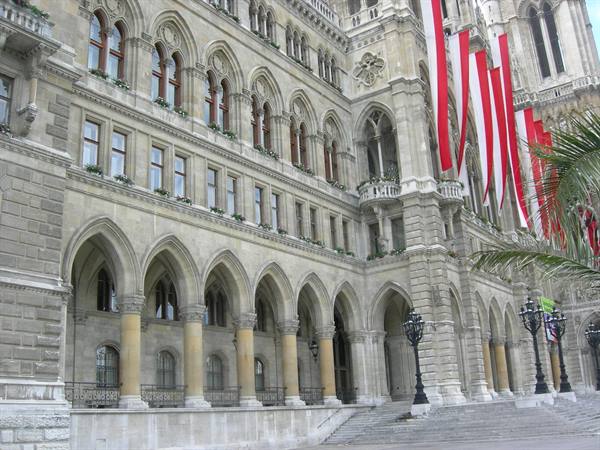 Neo-Gothic facade of Vienna Rathaus with arches, red-white banners and palms