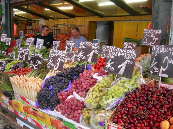 Market stall with grapes, cherries and asparagus, price signs, vendors under the canopy