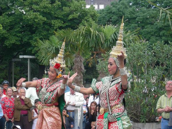 Two Thai dancers in golden costumes and headdresses perform before a crowd