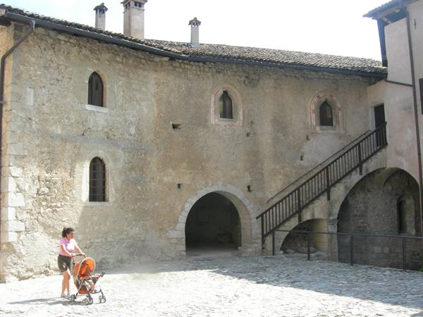 Stone courtyard of a medieval castle with outdoor staircase and a woman pushing a stroller