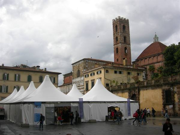 White event tents in Lucca square beneath the brick bell tower, cloudy sky