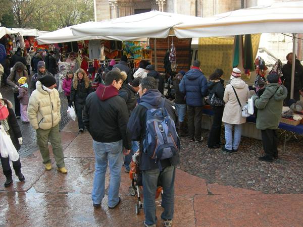 Crowded street market in a stone square, people browsing white canopy stalls