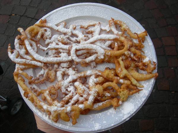 Fried funnel cake dusted with powdered sugar on a paper plate