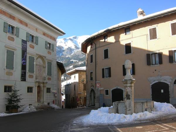 Mountain square with snowy stone fountain, old buildings and snowy mountain