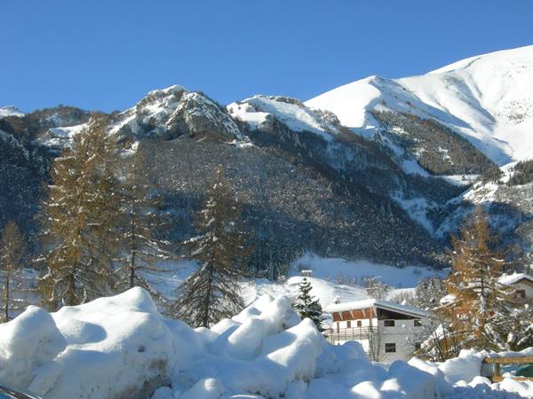 Snowy peaks above larches and wooden chalets, fresh snow on the ground