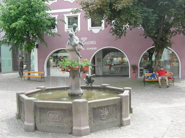 Stone fountain with putti statue and flowers in front of a pink building