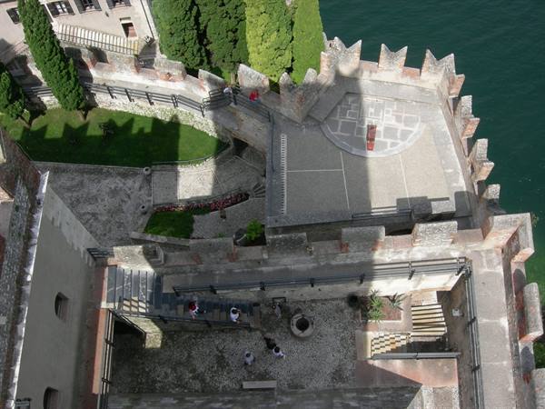 From the castle's crenellated walls above, tourists on stone stairs and paved courtyard